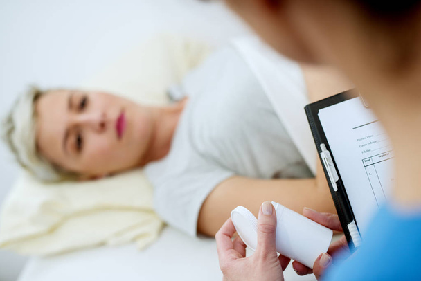 nővér gazdaság gyógyszert és papírok, női beteg kórházi ágyon  - Fotó, kép