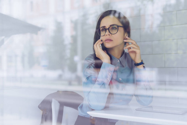 pensive young girl freelancer with glasses talking on the phone about business - Фото, изображение