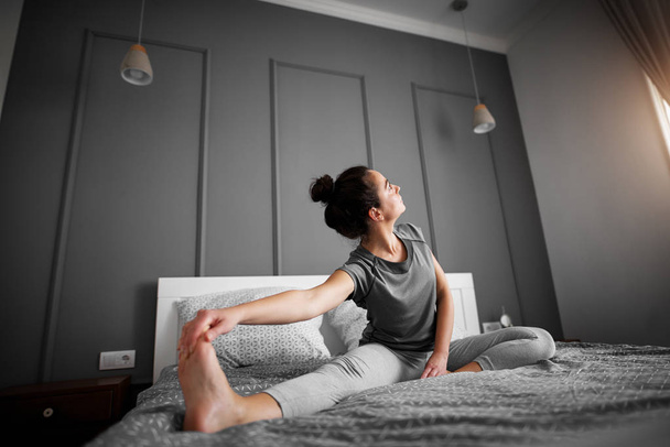 attractive sporty woman doing seated yoga pose in bed  - Fotografie, Obrázek