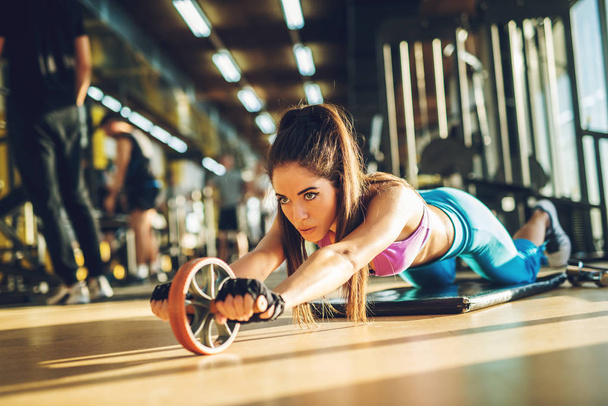 δραστήρια σπορ γυναίκα που κάνει άσκηση με abs ρόδα κυλίνδρων στο χαλί στο γυμναστήριο - Φωτογραφία, εικόνα