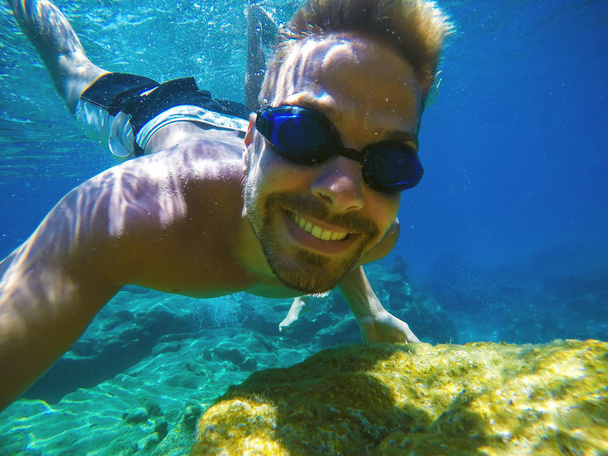 young man swimming underwater and taking selfie with selfiestick - Photo, Image