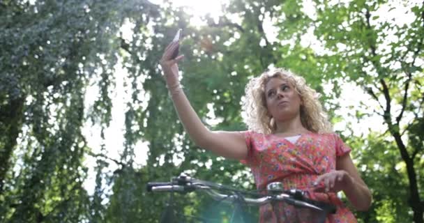 Young adult female taking selfie in park with bicycle - Кадры, видео