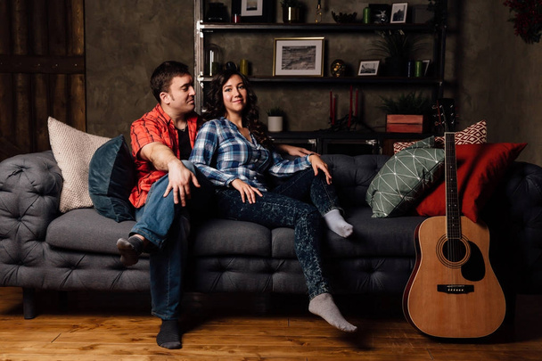 couple is sitting on the couch with a guitar. Long hair of a brunette with an acoustic guitar. - Photo, image