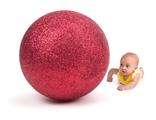 Cute Baby looking at a Huge Christmas Ornament on white - Photo, Image