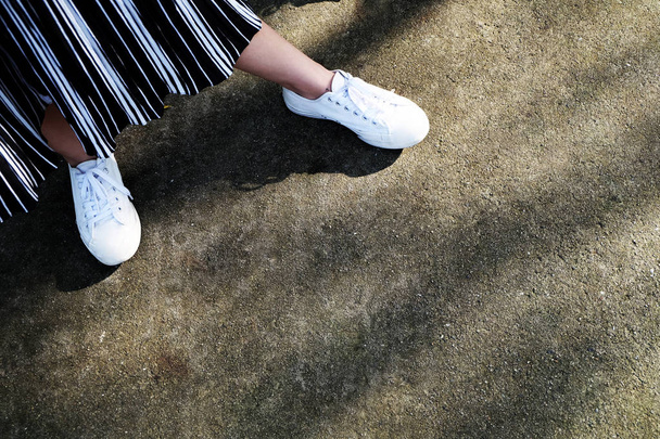 Buty trampki białe. Kobieta jest nogi w białe buty i spodnie na beton Street tło Świetne do dowolnego użytku. - Zdjęcie, obraz
