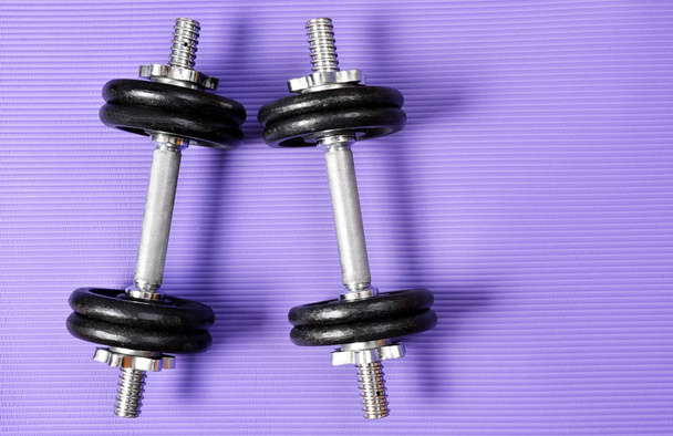 Black dumbbell on purple fitness mat. Exercise equipment. Healthy lifestyle concept. - Photo, Image