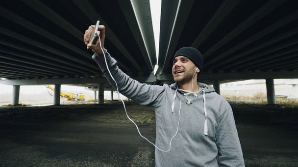 Athlete man having video chat on smartphone with his trainer after workout at urban location outdoors in winter - Фото, изображение