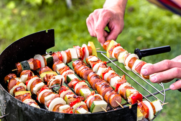 Grigliate di cibo alla griglia, mani che preparano spiedini con verdure e salsiccia, barbecue sull'erba, fuori concetto di festa estiva
 - Foto, immagini
