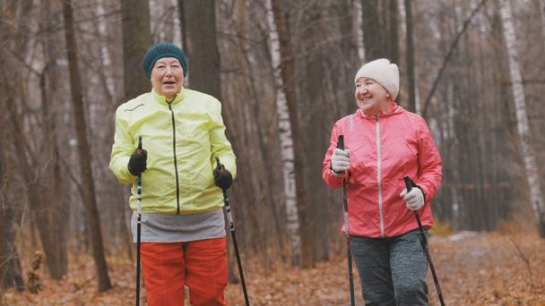 Dos ancianas en el parque de otoño tienen un entrenamiento moderno y saludable: caminar nórdico
 - Foto, Imagen