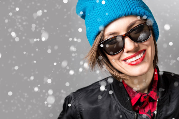 Young beautiful happy smiling girl over snowfall. Model wearing stylish outfit, closeup. empty space for text - Foto, Imagen