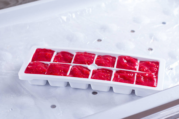 Bevroren bessen kubussen in een container in de vriezer - Foto, afbeelding