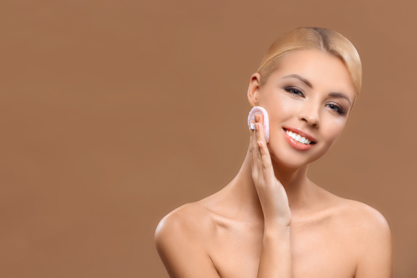 beautiful smiling woman with perfect skin applying makeup with powder puff, isolated on brown - Photo, Image