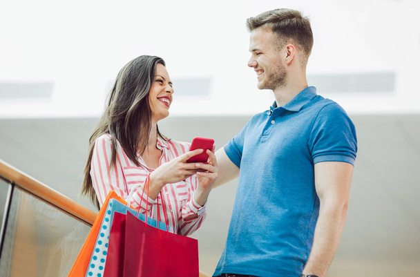 щаслива молода пара з сумками і смартфонами в торговому центрі
 - Фото, зображення
