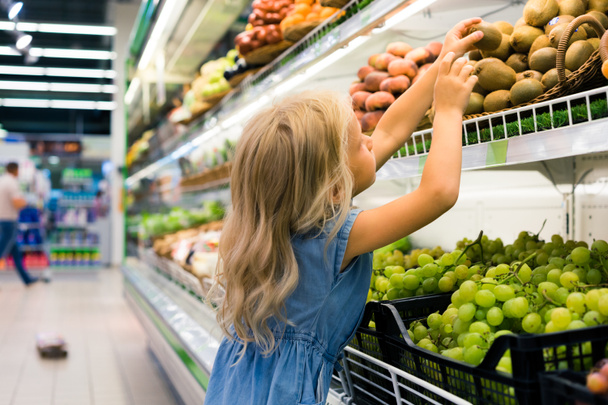 schattig vrouwelijke kind kiezen van fruit in de supermarkt - Foto, afbeelding