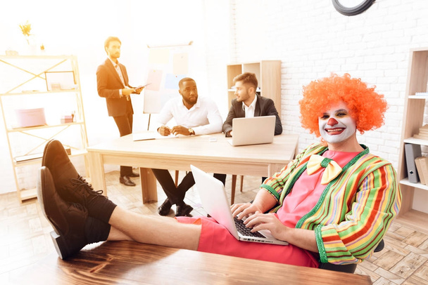 A man in a clown suit sitting at his desk, his feet up on the table. - Photo, image