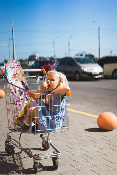 little female child eating chips while sitting in shopping cart with skateboard - 写真・画像