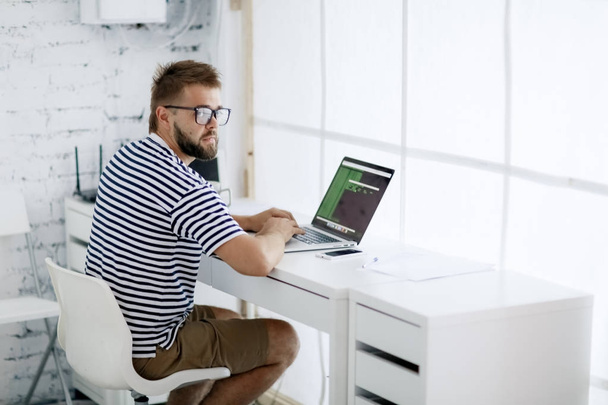 fiatal jóképű üzletember gépelés-on laptop ül a modern irodai íróasztal - Fotó, kép