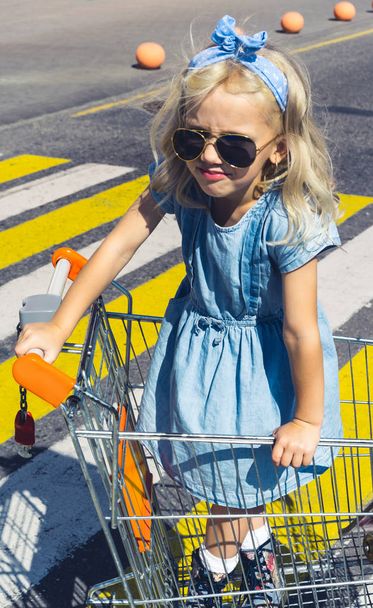 little adorable kid in sunglasses having fun in shopping cart on crosswalk - Zdjęcie, obraz