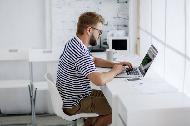 молодий чоловік сидить за столом, працюючи на ноутбуці в сучасному офісі
 - Фото, зображення