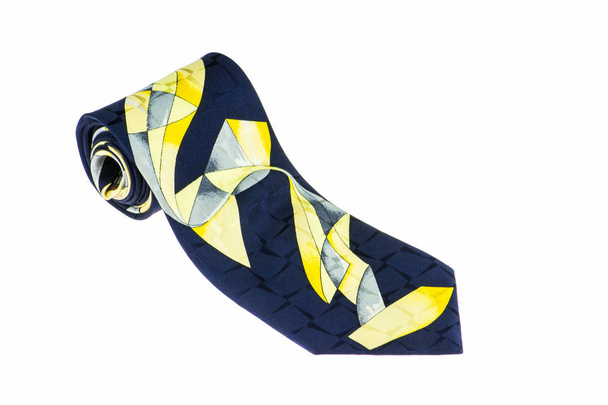 Close-up van een elegante stijlvolle band gerold en geïsoleerd op een witte achtergrond, donker blauwe stropdas met abstracte geel patroon - Foto, afbeelding
