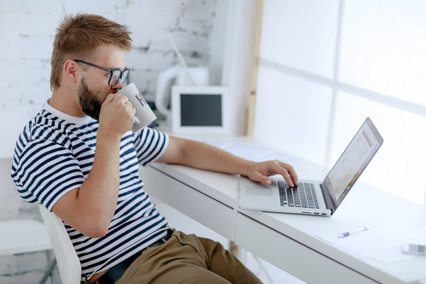 jeune homme d'affaires beau travail sur ordinateur portable assis au bureau et boire du café dans le bureau
 - Photo, image