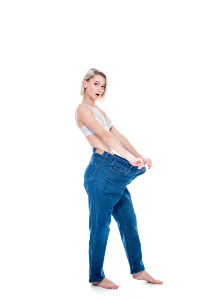 shocked girl showing weight loss by wearing old jeans, isolated on white - Valokuva, kuva