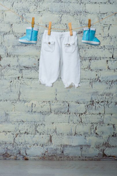 Дитячі черевики і колготки сухі на мотузці на білій цегляній стіні
. - Фото, зображення