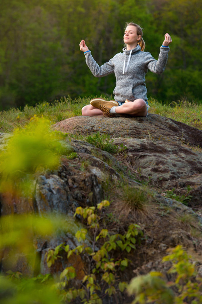 Menina de ioga com vista para a floresta, com luz solar. Jovem em lótus posar sentado na pedra. Conceito de calma e meditação
. - Foto, Imagem