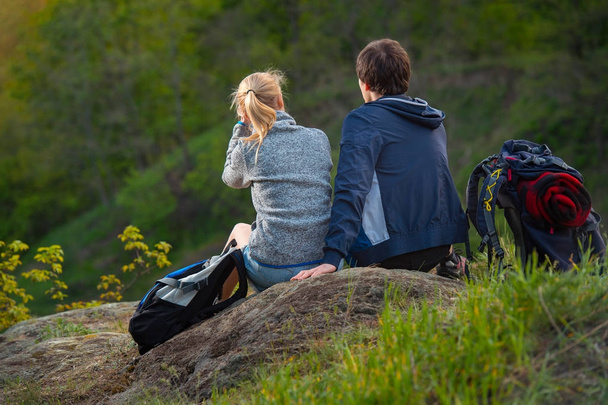 Dva turisté s batohy sedět a odpočívat. Pohled zezadu. Cestování, dovolené, prázdnin a dobrodružství koncept. Lesní horské krajiny pozadí - Fotografie, Obrázek