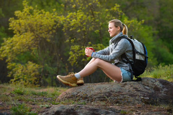 紅茶のカップと残りの部分を持っている女性バックパッカー夏の森でのハイキングと停止します。旅行、ハイキング、バック パッキング、観光、人々 の概念 - 写真・画像