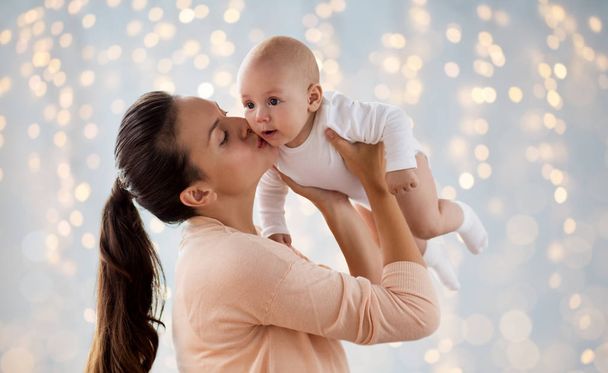 happy mother kissing little baby boy over lights - Photo, Image