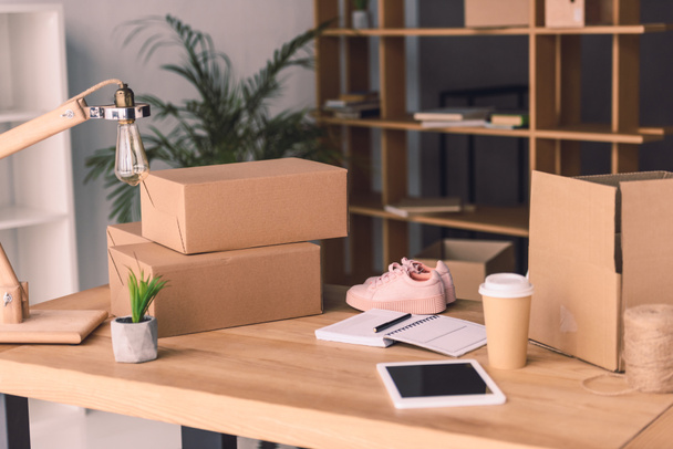 freelance worker workplace with cardboard boxes, notebook and pair of shoes at home office - Zdjęcie, obraz