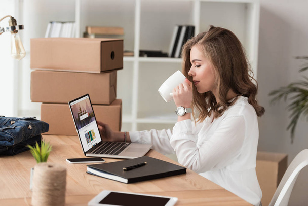 Seitenansicht einer Geschäftsfrau, die Kaffee trinkt, während sie am Laptop am Tisch arbeitet - Foto, Bild