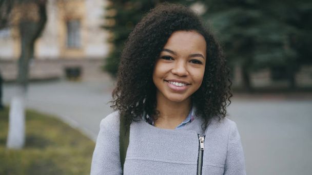 Portret van gemengd ras krullend student meisje glimlachend in de camera en lachen op straat - Foto, afbeelding