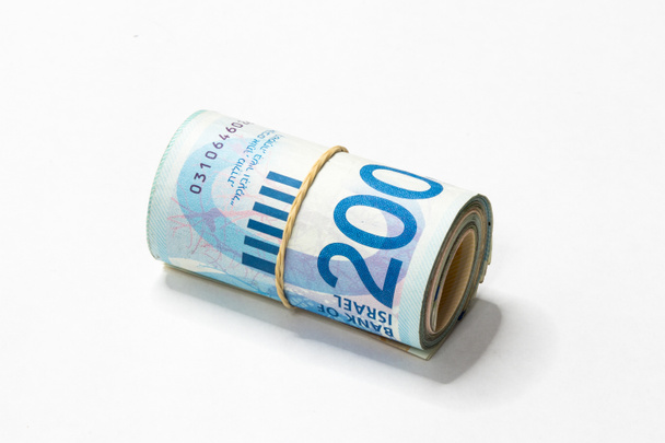 Um bando de notas de dinheiro israelenses New Shekels (NIS) enroladas e mantidas em conjunto com uma faixa de borracha simples isolada em um fundo branco
. - Foto, Imagem