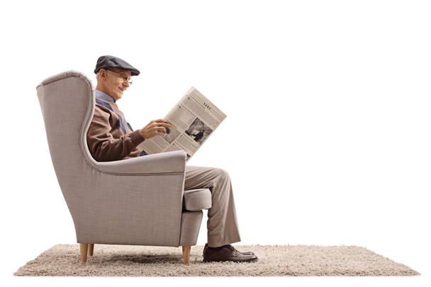 Senior seated in an armchair reading a newspaper - Photo, image