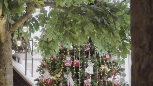 Grußsaisonkonzept. Gimbal Shot von Ornamenten auf einem großen Weihnachtsbaum mit dekorativem Licht und fallendem Schnee in 4k (uhd) - Filmmaterial, Video