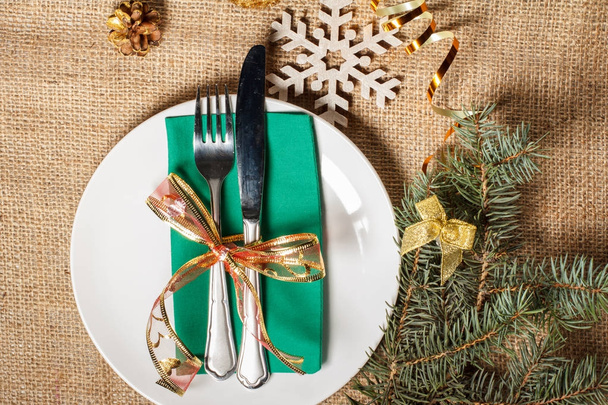 Нож и вилка на зеленой салфетке и белой тарелке, декоративный снег
 - Фото, изображение