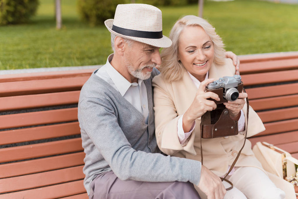 Two pensioners are sitting on the bench and studying a vintage camera. They are going to take a few photos - Foto, immagini