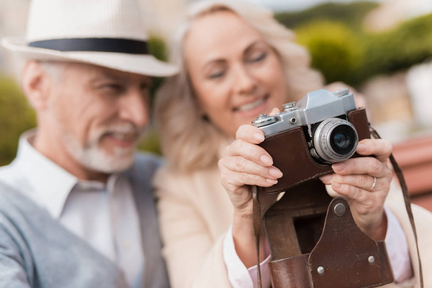 Two pensioners are sitting on the bench and studying a vintage camera. They are going to take a few photos - Foto, Imagem