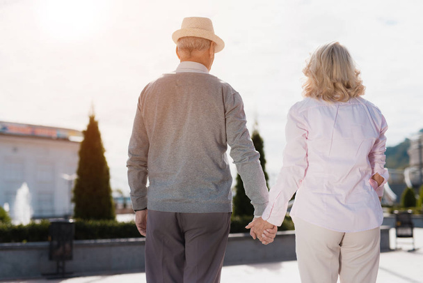 An elderly couple is walking around holding hands. They walk along a beautiful square - Valokuva, kuva