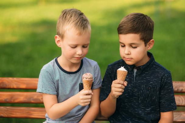Két gyermek játszik a parkban. Két gyönyörű fiú póló és rövidnadrág szórakozást, mosolyogva. Ők eszik fagylaltot, ugrás, fuss. Nyár sunny - Fotó, kép