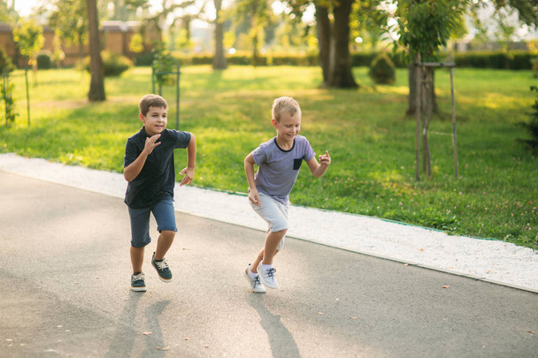 Kaksi lasta leikkii puistossa. Kaksi kaunista poikaa T-paidoissa ja shortseissa pitää hauskaa hymyillen. He syövät jäätelöä, hyppivät, juoksevat. Kesä on aurinkoinen
 - Valokuva, kuva