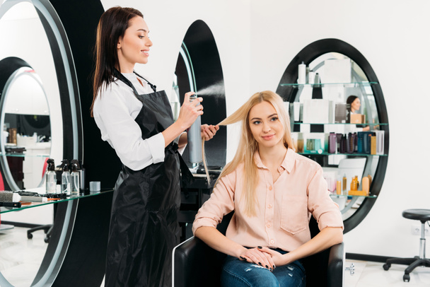smiling hairdresser applying hair spray  - Zdjęcie, obraz