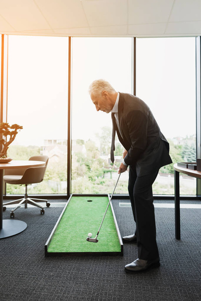 A man in a strict business suit plays in an office in a mini-golf - Foto, Bild