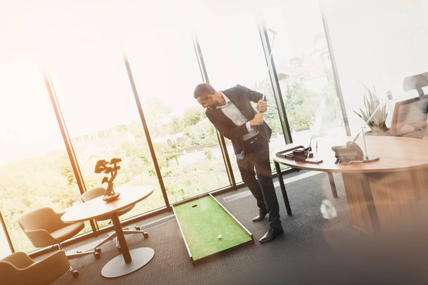A man in a strict business suit plays in an office in a mini-golf - Fotografie, Obrázek