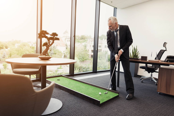 Een man in een strikte pak speelt in een kantoor in een mini golf - Foto, afbeelding