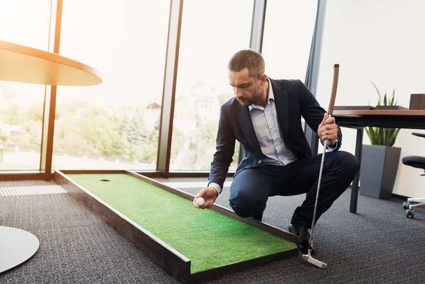 A man in a strict business suit plays in an office in a mini-golf - Photo, Image