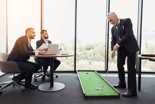 В то время как директор играет в гольф в офисе, подчиненные приходили к нему с отчетами. Они сидят и смотрят, как он играет.
 - Фото, изображение