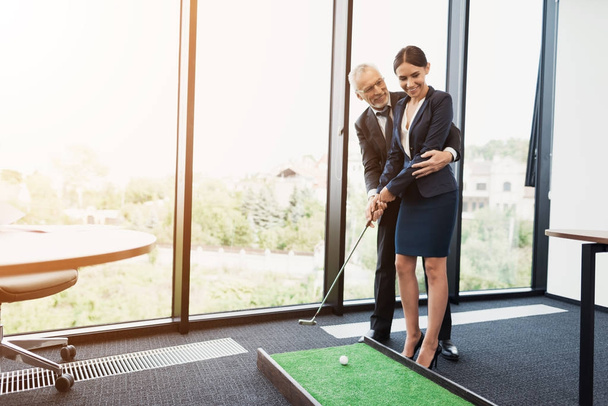 An elderly man is teaching his secretary to play mini golf. He directs her - 写真・画像